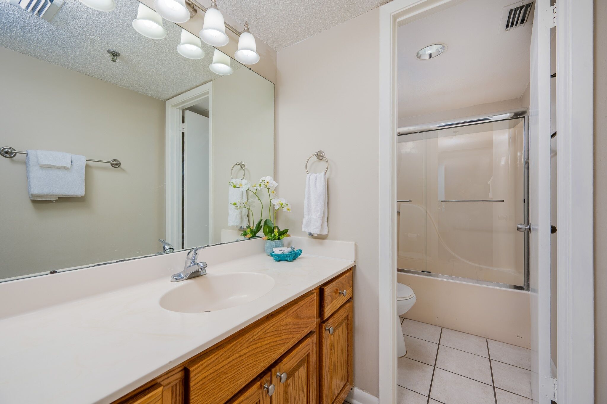 A bathroom with a large mirror, a sink, wooden cabinets, a toilet, and a glass-enclosed shower.
