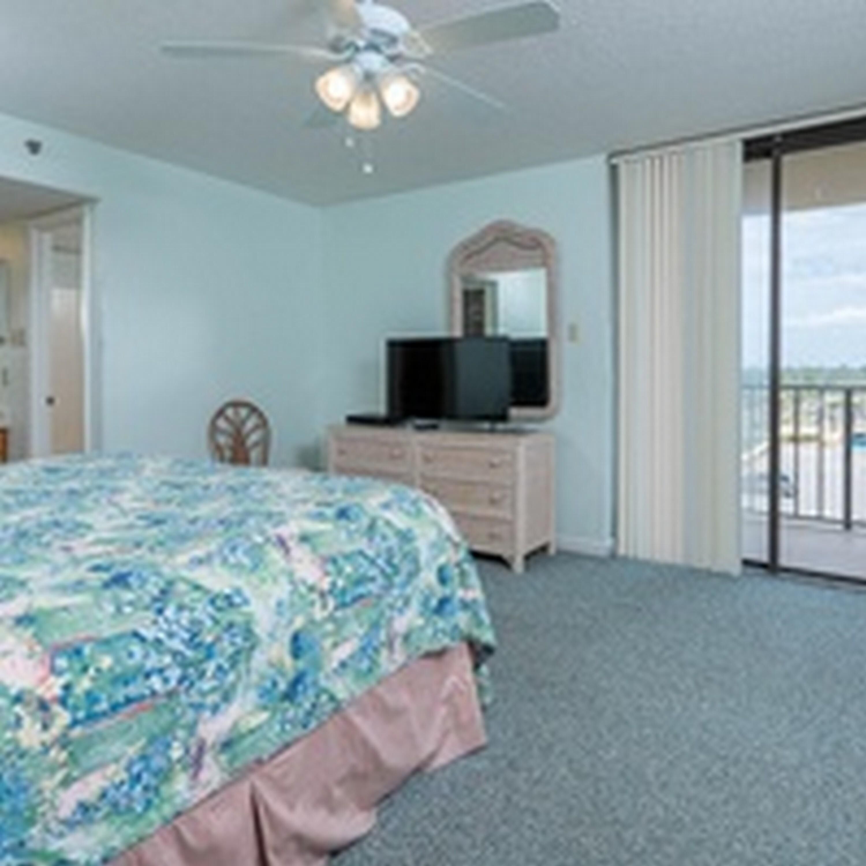A bedroom with a bed, a dresser, a television, and a ceiling fan.
