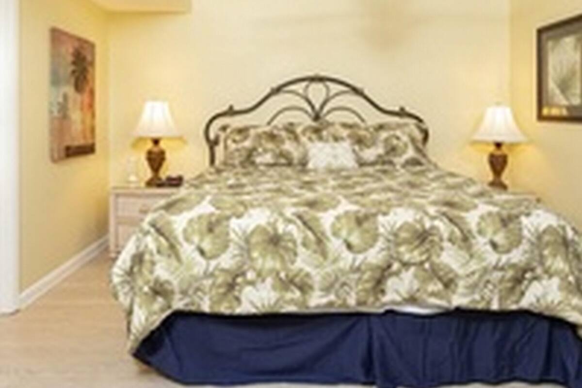 Un dormitorio con una cama, dos lámparas de noche, un ventilador de techo y un cuadro en la pared.