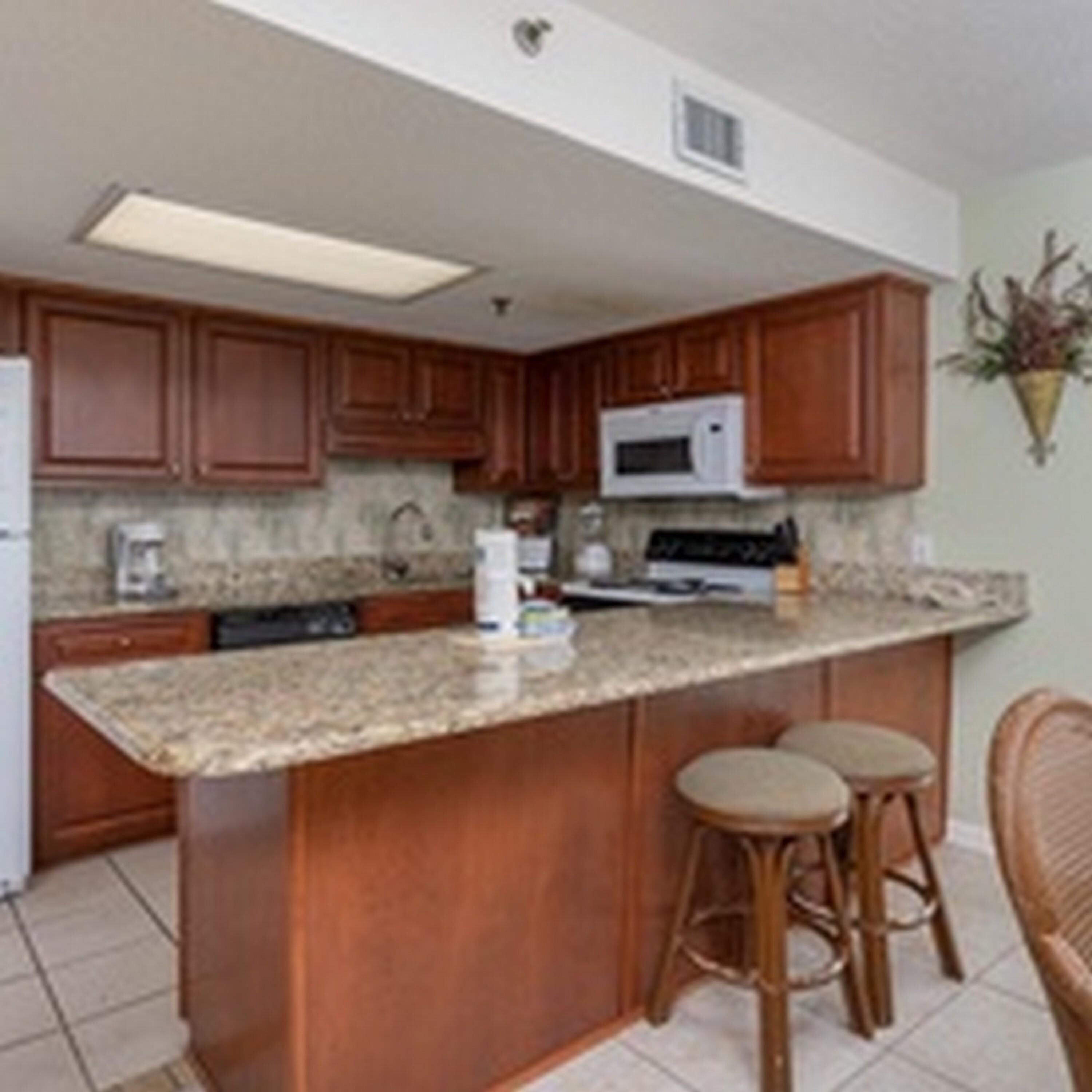 A kitchen with wooden cabinets, a granite countertop, a microwave, and a sink.