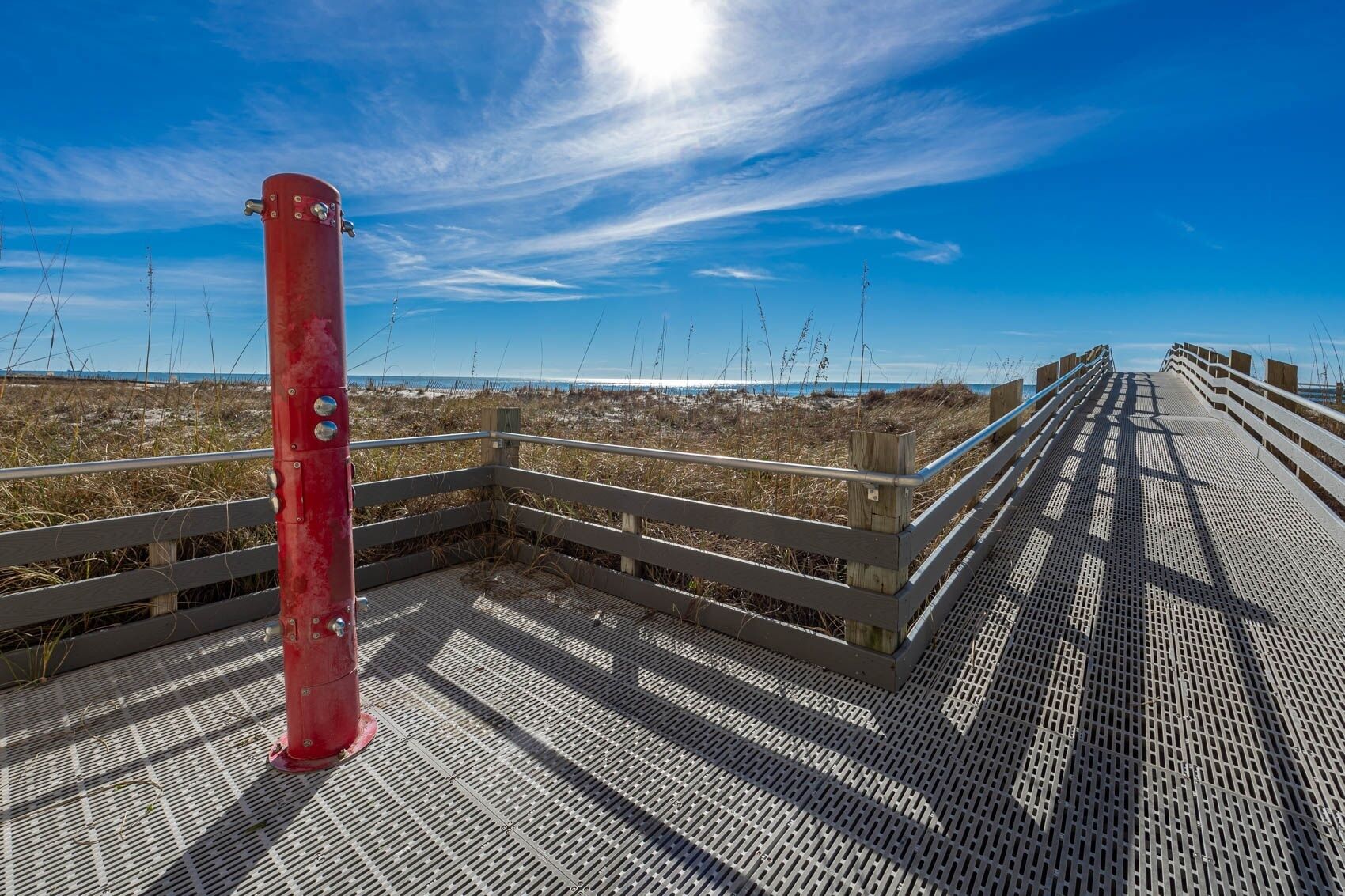 A wooden boardwalk with a metal railing, leading to a beach with sparse vegetation.