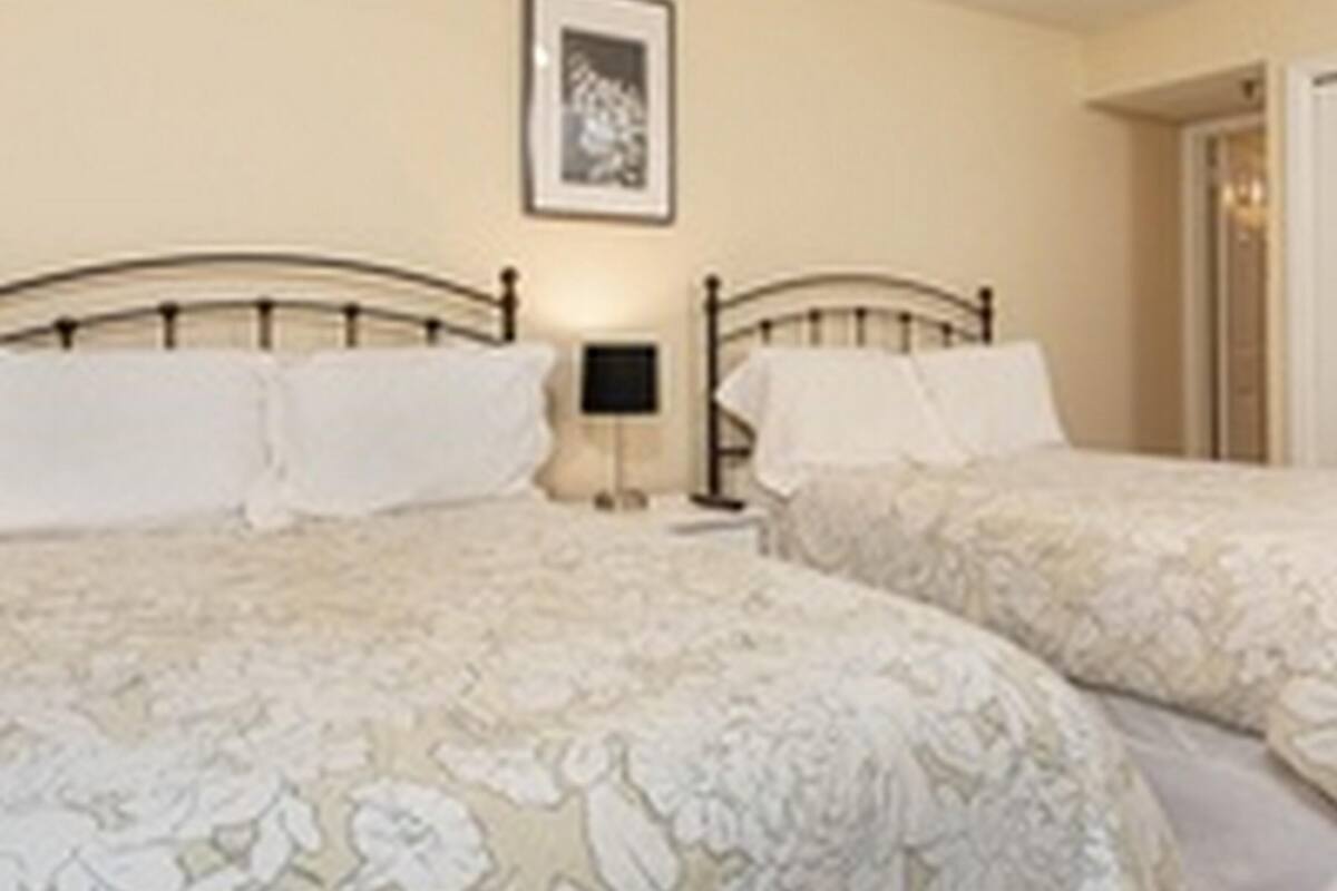 Habitación de hotel con dos camas, cada una con cubrecama floral, una mesita de noche con lámpara y un cuadro enmarcado en la pared.