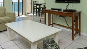 Sala de estar com sofá, mesa de centro, TV em um suporte de madeira e vista para o mar através da porta de vidro.