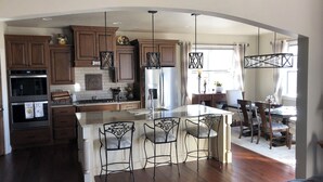 A spacious kitchen with wooden cabinets, a central island with bar stools, and a dining area with a chandelier. - Plan for EAA ! Executive ranch, only 13 miles away  (Neenah)