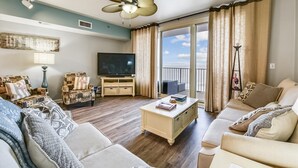 A living room with a television, two sofas, a coffee table, and a balcony with curtains. - Shores of Panama 2326 - 1 Bedroom + Bunks . Reserved Parking! 1 Condo by RedAwning (Panama City Beach)