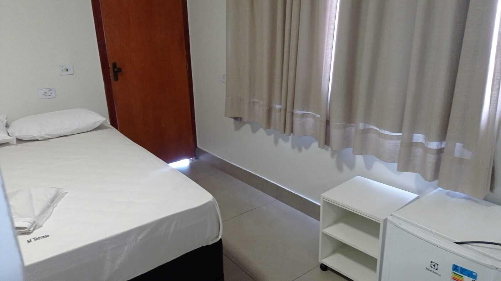Une petite pièce propre, comprenant un lit, une table de chevet, une commode et un petit placard.