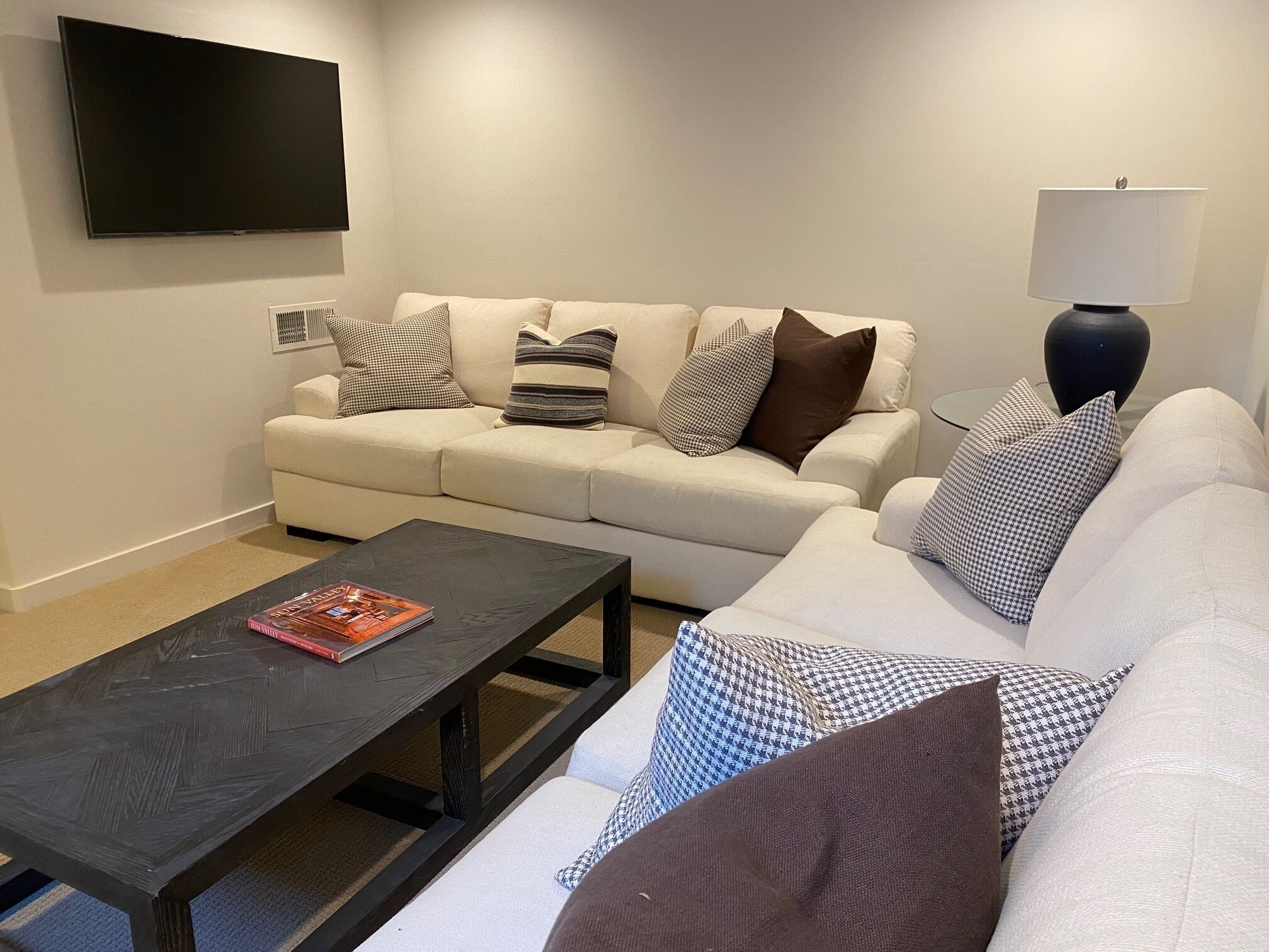 Una sala de estar con un sofá, una mesa de centro, una lámpara y un televisor de pantalla plana montado en la pared.