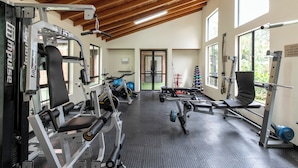 Ett gym med olika typer av träningsutrustning, stora fönster och ett högt trätak.