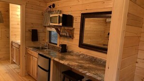 Une cuisine compacte aux murs en bois, dotée d’un four à micro-ondes encastré, d’un évier et d’un réfrigérateur.