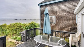 A wooden deck with a glass table and chairs, overlooking a body of water. - Massachusetts Vacation Rental: 5 Mi to Fall River (Somerset)