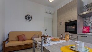 A modern living room with a sofa, a dining table with a yellow placemat, and a kitchen area with an oven and a clock on the wall. - La Casetta di Dado by Wonderful Italy (Turin)