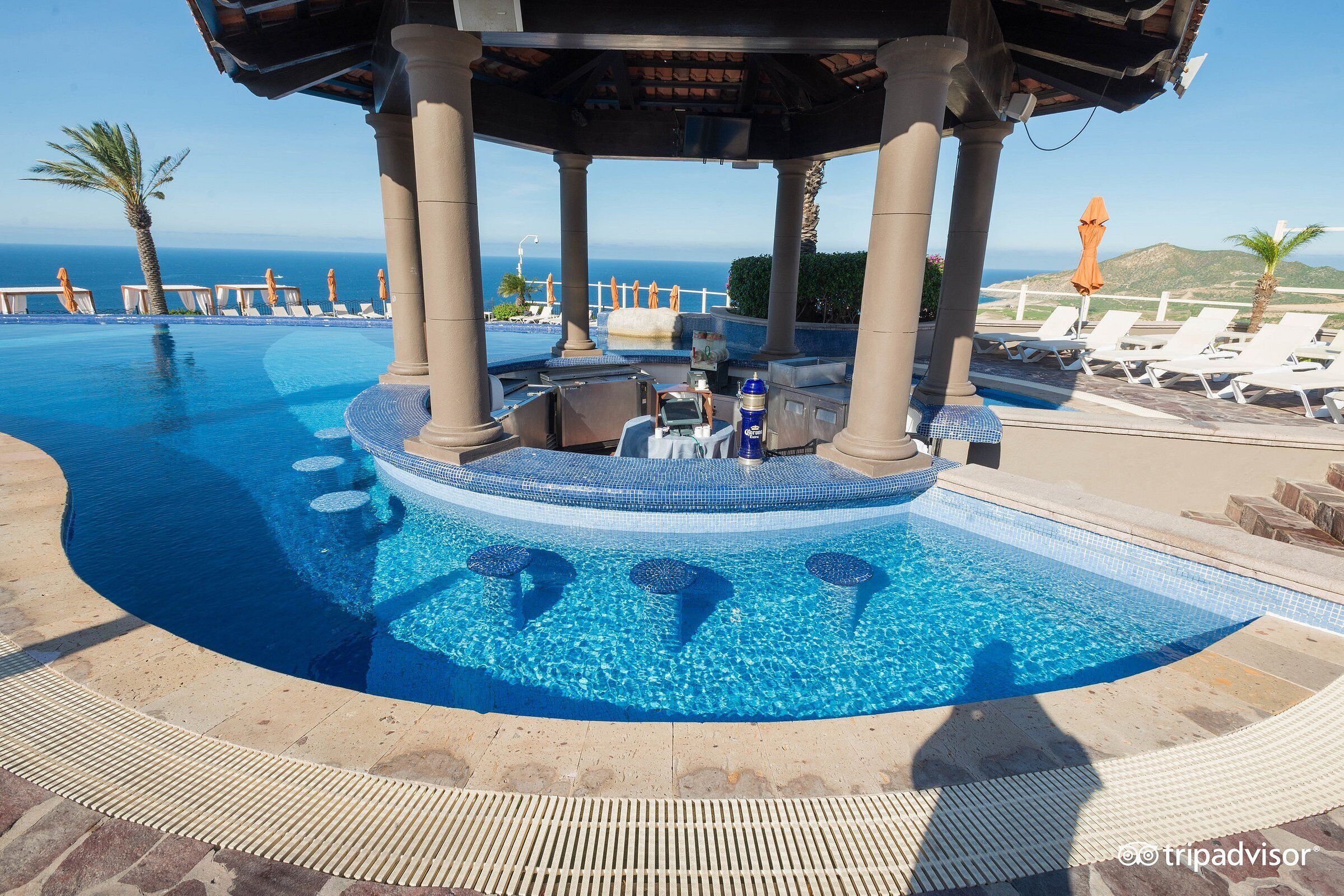 A pool area with lounge chairs, a hot tub, and a view of the ocean.