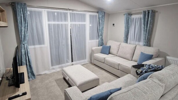 Una sala de estar con un sofá beige, un reposapiés a juego y un televisor sobre un mueble de madera.