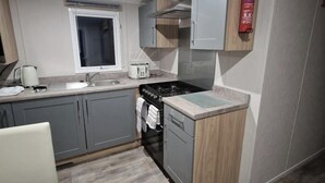 Una cocina compacta con gabinetes grises, una estufa a gas, un lavamanos y una ventana.
