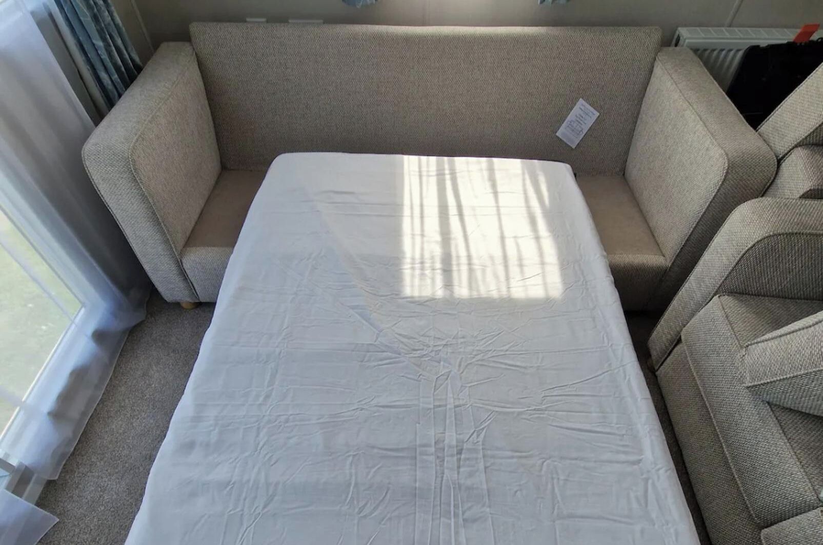 A room with a beige sofa and a white mattress on the floor.