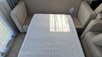 A room with a beige sofa and a white mattress on the floor.