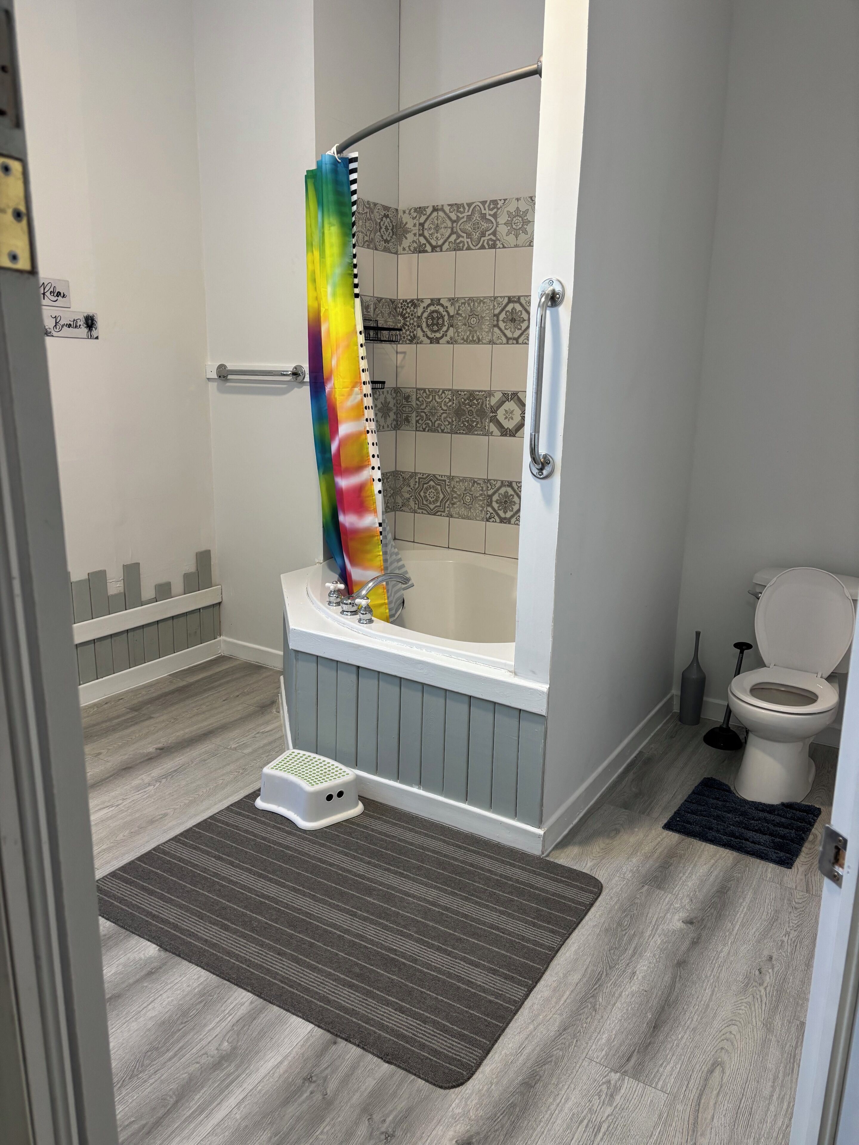 A bathroom with a shower, toilet, and a small step stool.