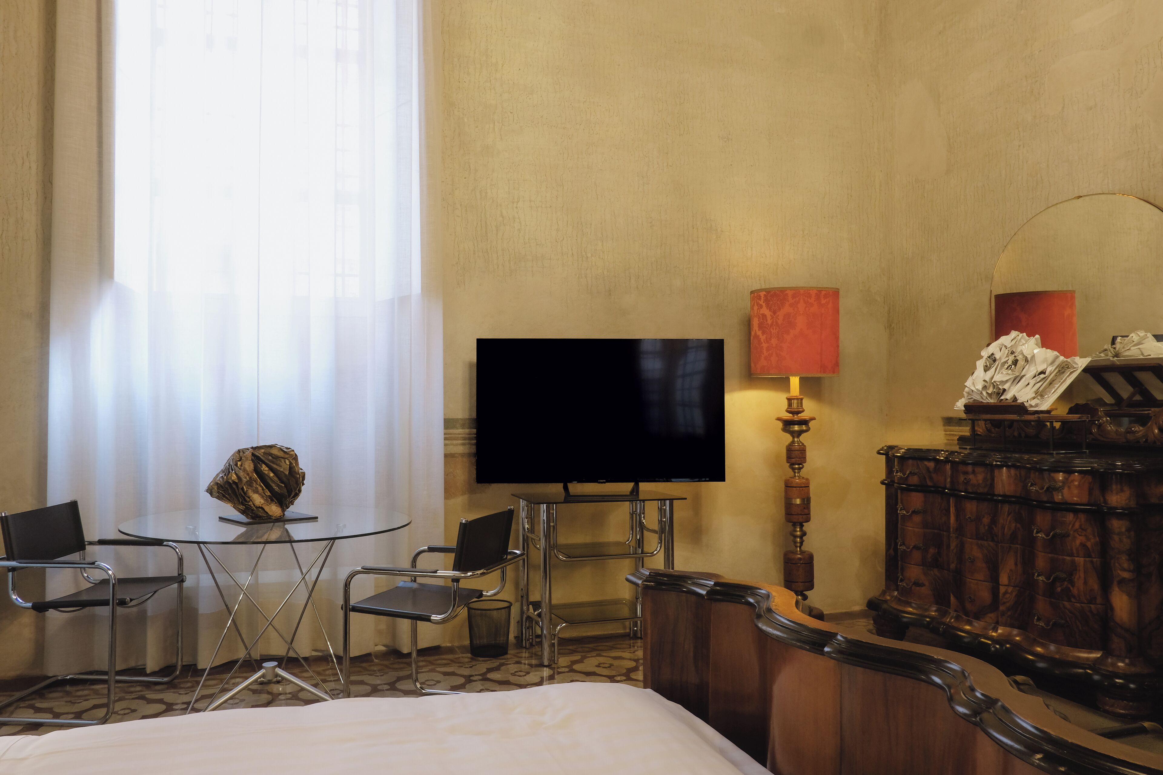 Ein Hotelzimmer mit einem Bett, einem Fernseher, einem Glastisch mit Stühlen, einer Lampe und einem Holzschrank.
