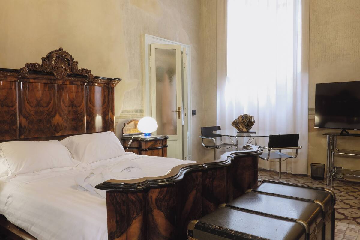 A hotel room with a wooden bed, a desk with a lamp, a television, and a chair.