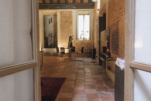 A spacious room with a brick wall, a large window, a fireplace, and a dining area with chairs and a table. - Palazzo Guazzoni Zaccaria (Cremona)