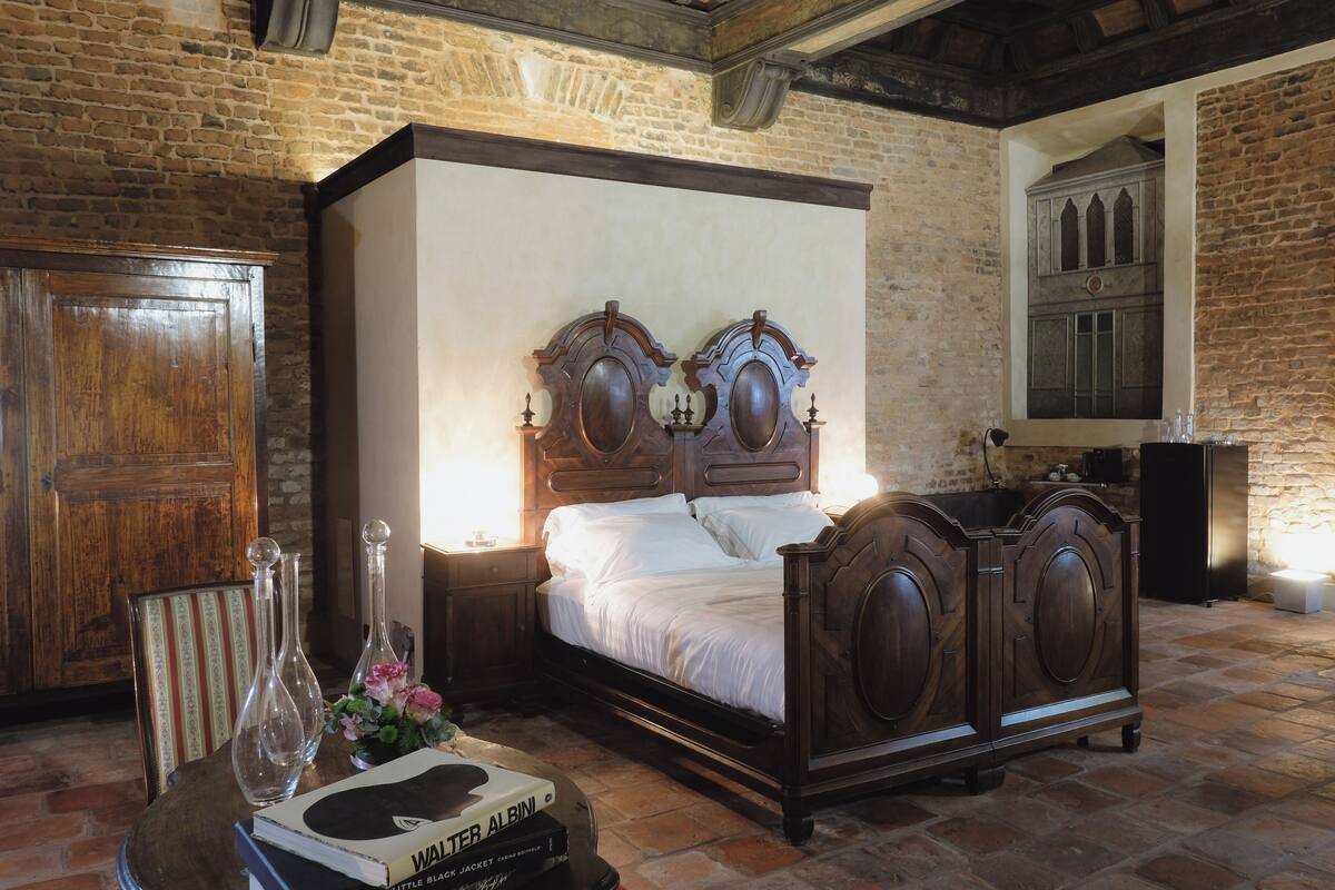 A bedroom with a four-poster bed, wooden furniture, and a brick wall.
