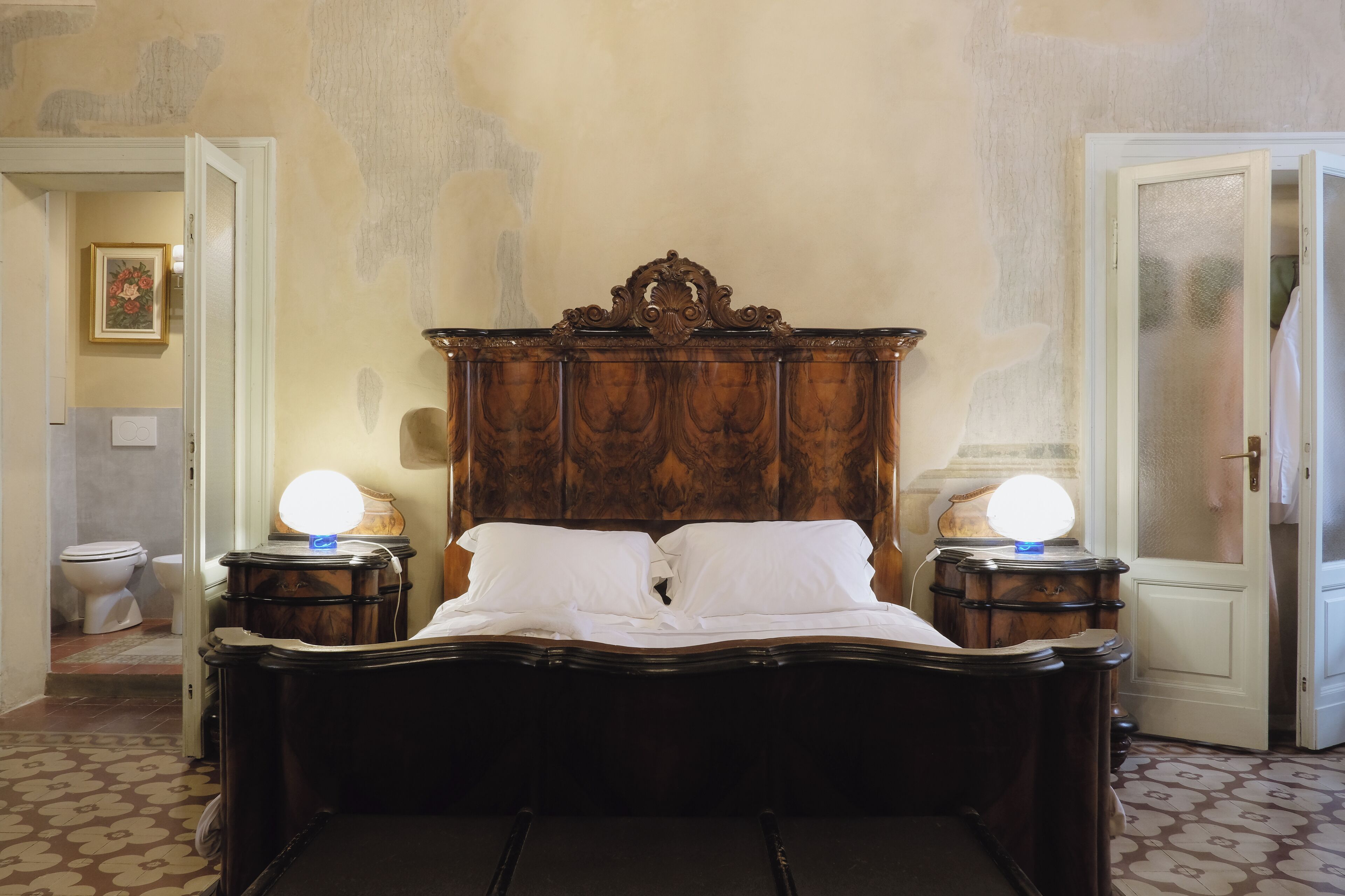 Ein Schlafzimmer mit einem hölzernen Bett, zwei Nachttischlampen und einer Tür zu einem anderen Raum.