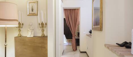 A hallway with a lamp, candelabras, a statue, a mirror, and a pair of shoes on a ledge.