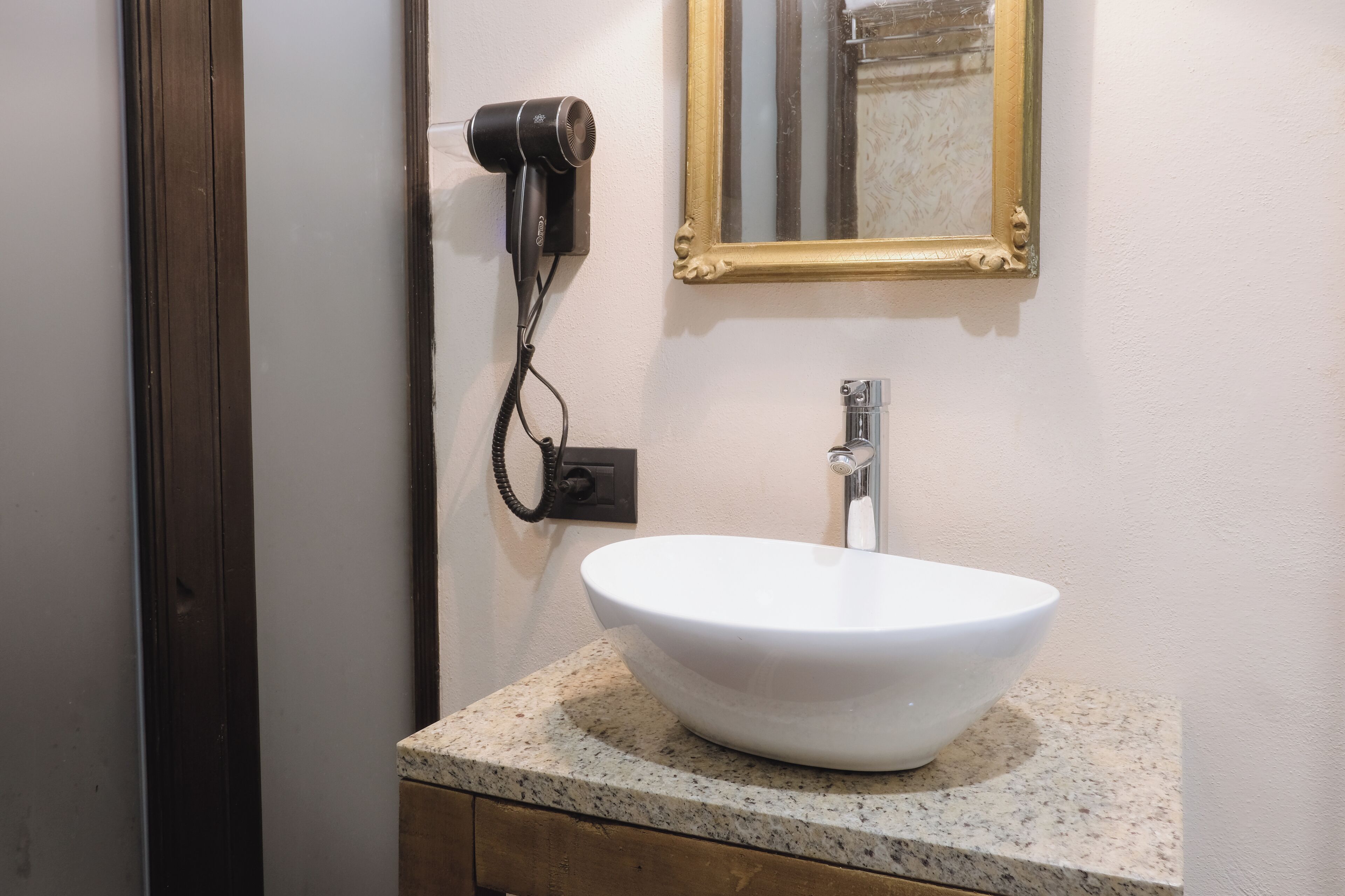 Un baño con un lavamanos blanco, un secador de pelo y un espejo con marco dorado.