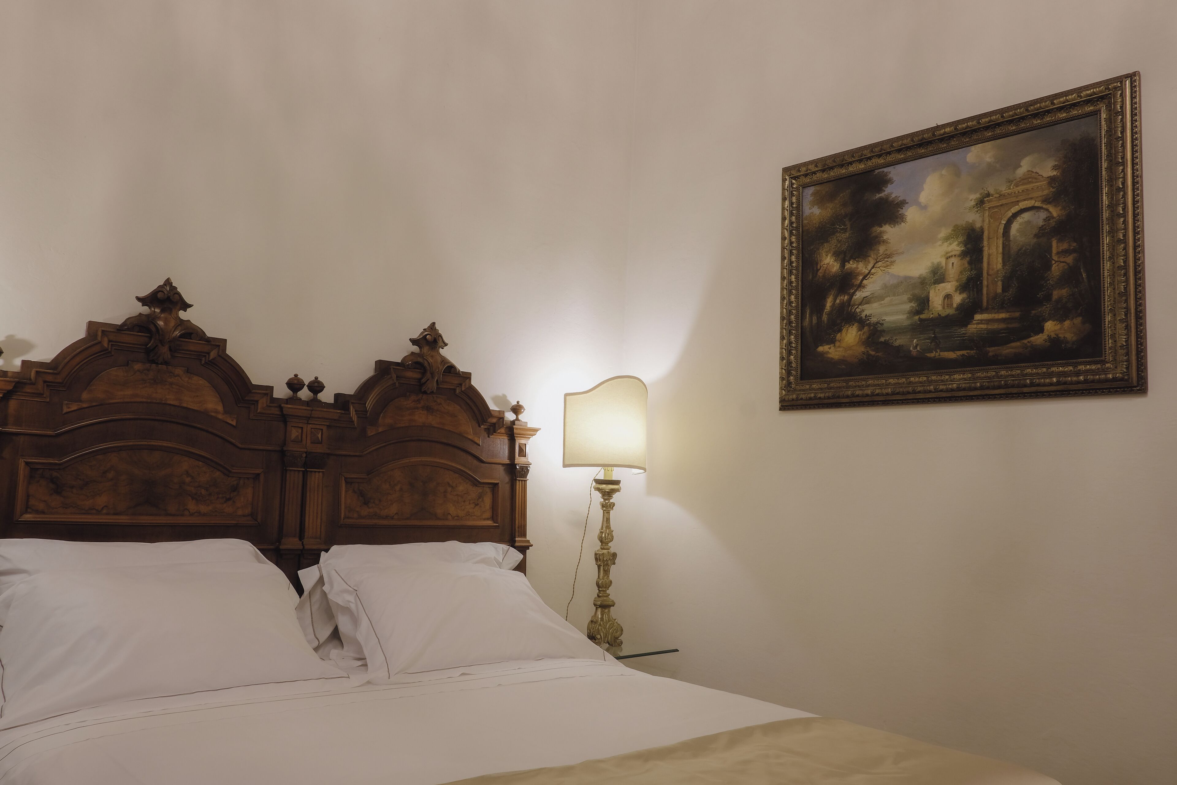 A bed with a wooden headboard, a bedside lamp, and a framed painting on the wall.