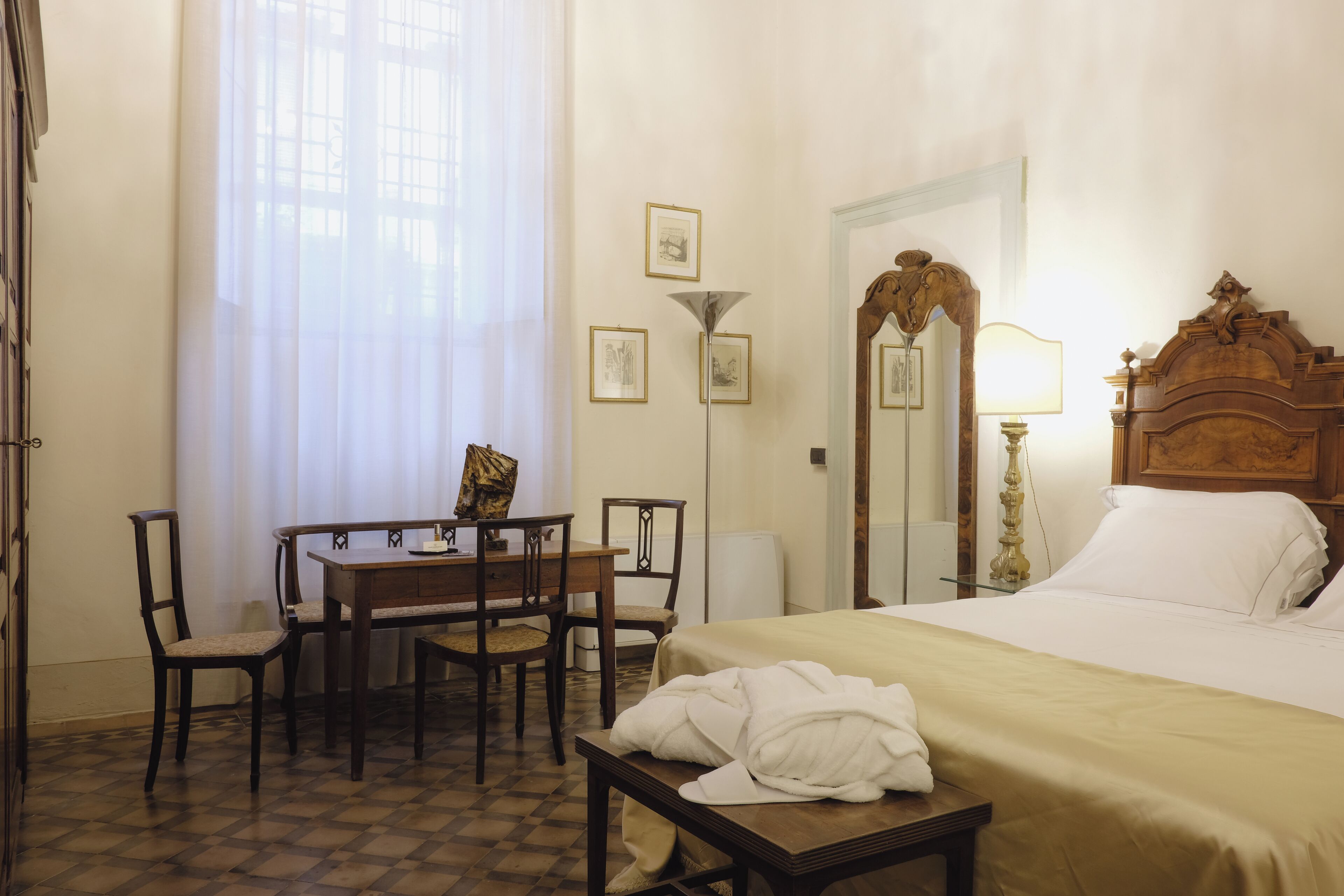 Une chambre d’hôtel avec un lit, un bureau avec des chaises, une lampe et des tableaux encadrés au mur.