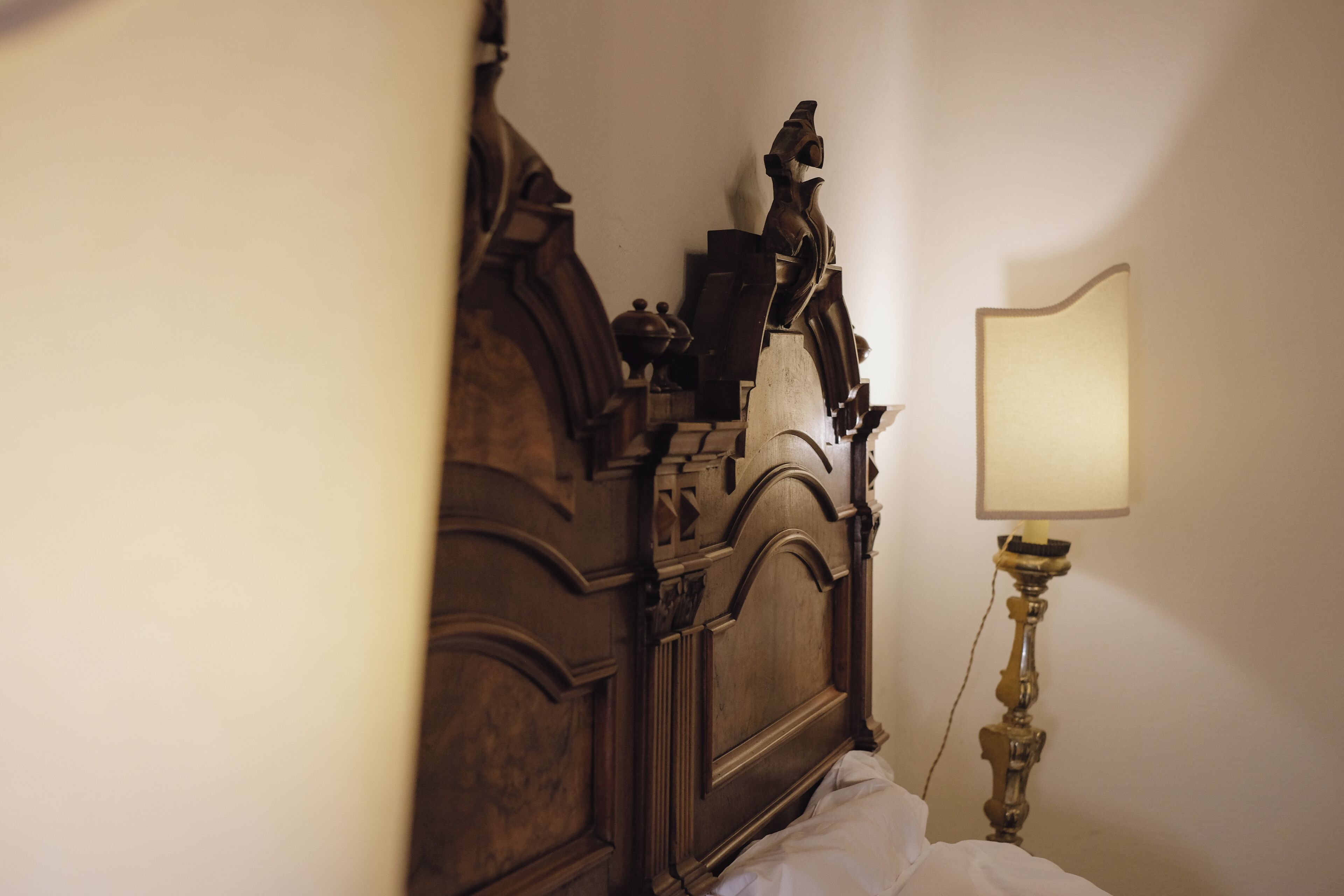 A wooden bed with a headboard, a bedside table with a lamp, and a wall-mounted shelf.