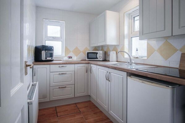 A compact kitchen with white cabinets, a microwave, a kettle, and a sink. - Rose Cottage - 3 Bed Cottage - New Hedges - Tenby (Tenby)