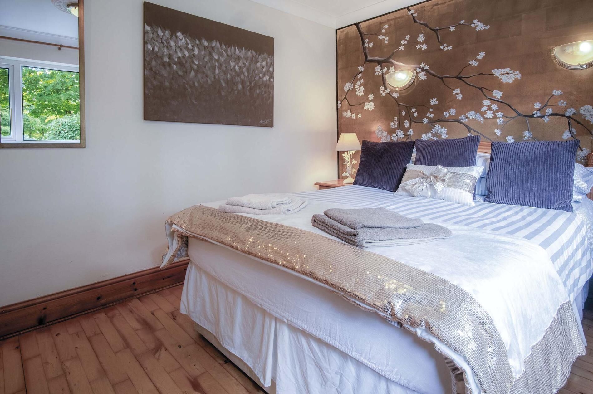 A bedroom with a large bed, a wooden headboard with a floral design, and a window with a view of trees.