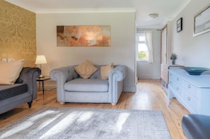 A living room with a grey sofa, a smaller grey armchair, a blue dresser, and a large abstract painting on the wall.