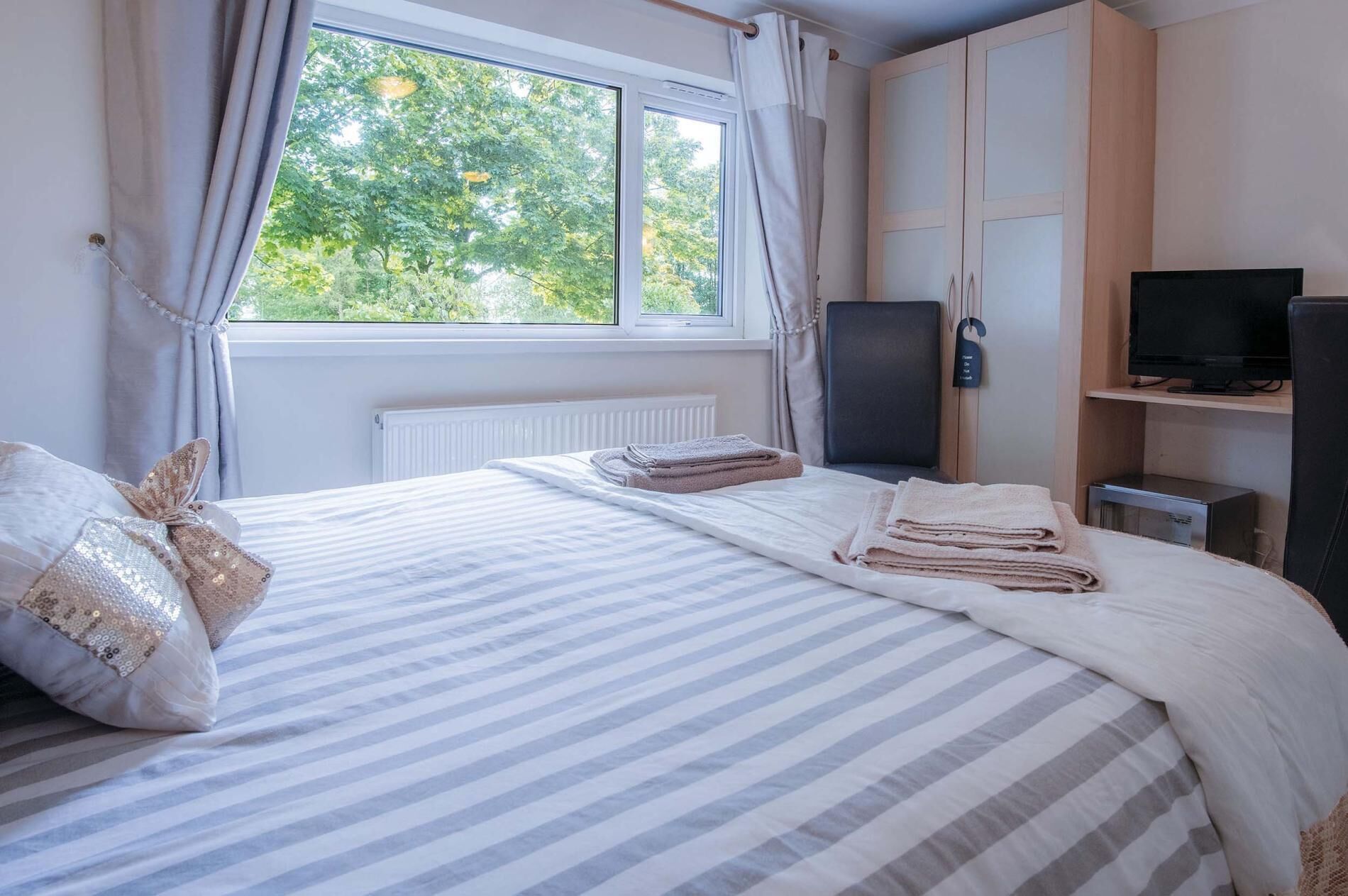 A hotel room with a bed, a TV, a desk, and a window with curtains.