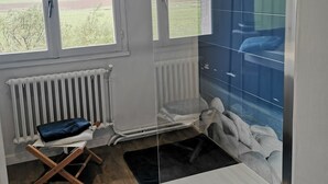 Een kamer met uitzicht op het landschap, een radiator, een opvouwbare stoel en een bed met een blauwe muur.