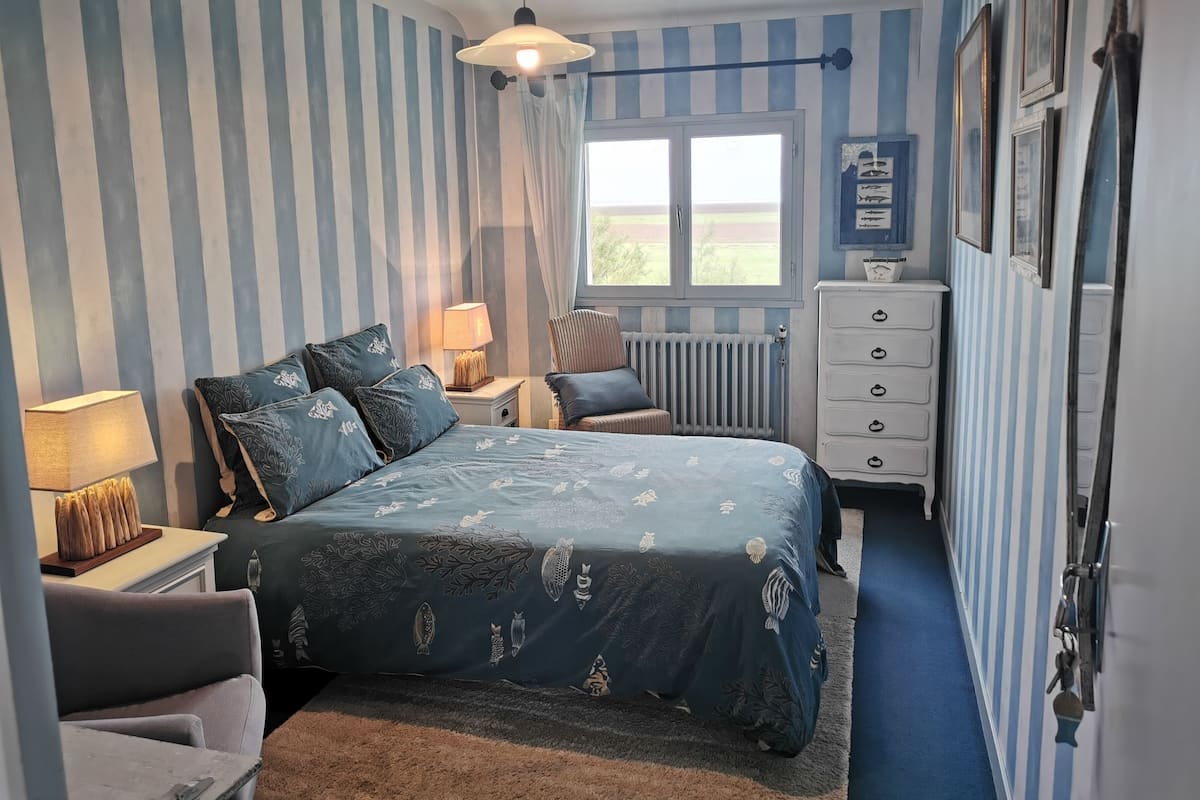 Et soveværelse med seng, natborde, kommode, radiator og et vindue med gardiner.