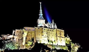 Une vaste structure imposante, rappelant un château, illuminée et dotée de nombreuses tours ainsi que d’une flèche proéminente.