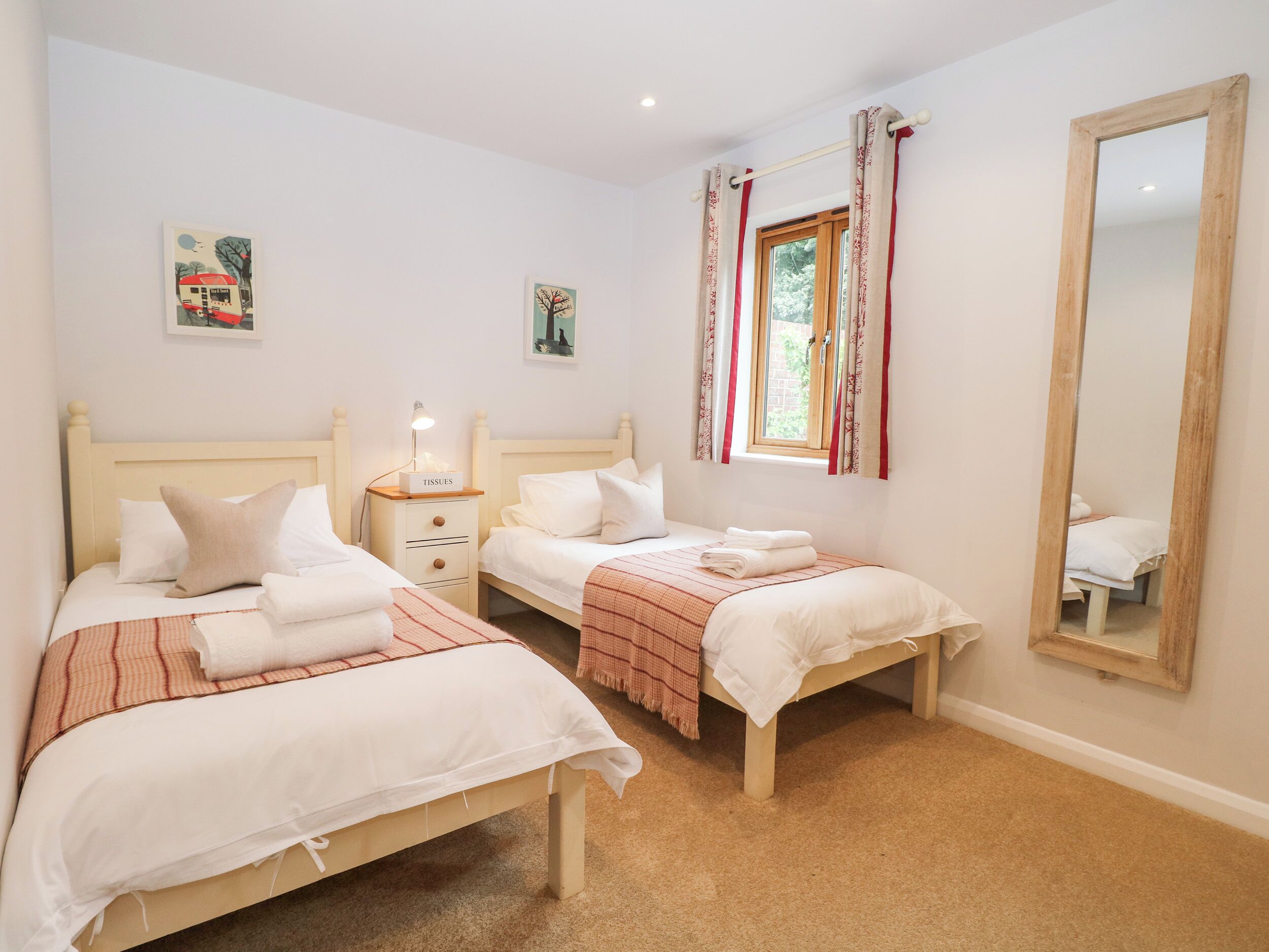 A bedroom with two beds, a bedside table with a lamp, a mirror, and artwork on the walls.