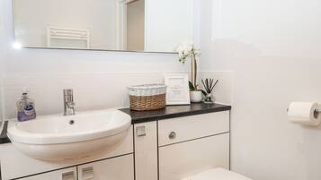 Un baño con lavamanos blanco, un espejo, un inodoro y una nota enmarcada sobre el mostrador.