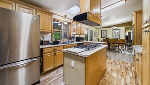 A kitchen with wooden cabinets, a stainless steel refrigerator, a central island with a stove, and a skylight. - Explore Redwood National Park with Hot Tub, Wood Stove, and Fire Pit! (Orick)
