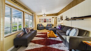 A spacious living room with a large window, a wooden coffee table, and a red and white rug. - Explore Redwood National Park with Hot Tub, Wood Stove, and Fire Pit! (Orick)