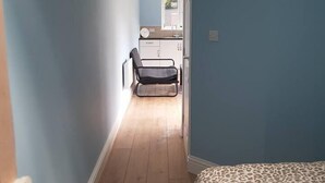 A narrow hallway with wooden flooring leading to a bedroom with a leopard print bedspread. - Cozy Studio in Luton (Luton)