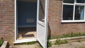 A house with a door open to a room with a radiator, a window, and a small garden area. - Cozy Studio in Luton (Luton)