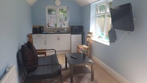 A compact living space with a kitchenette, a dining area, and a seating area with a sofa and a chair. - Cozy Studio in Luton (Luton)
