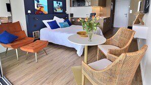 Une chambre d’hôtel moderne avec un lit, un fauteuil orange, des chaises en osier, une petite table et des œuvres d’art accrochées au mur.