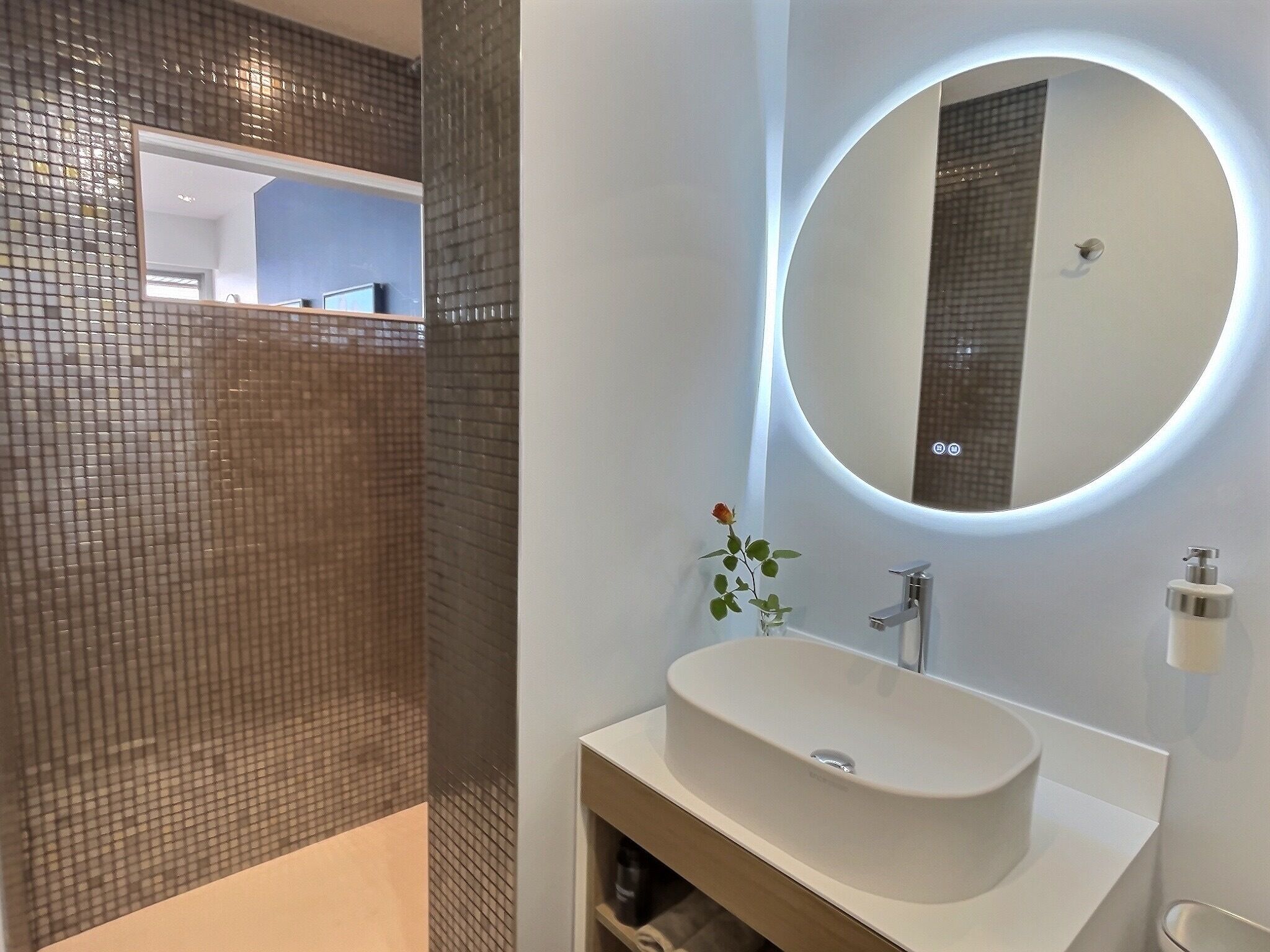 A modern bathroom with a large mirror, a white sink, and a small plant.