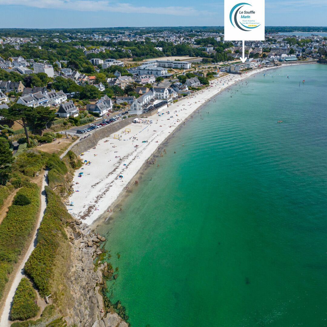Eine Luftaufnahme einer Küstenstadt mit einem langen Sandstrand, klarem türkisblauem Wasser und einer Mischung aus Wohn- und Geschäftsgebäuden.