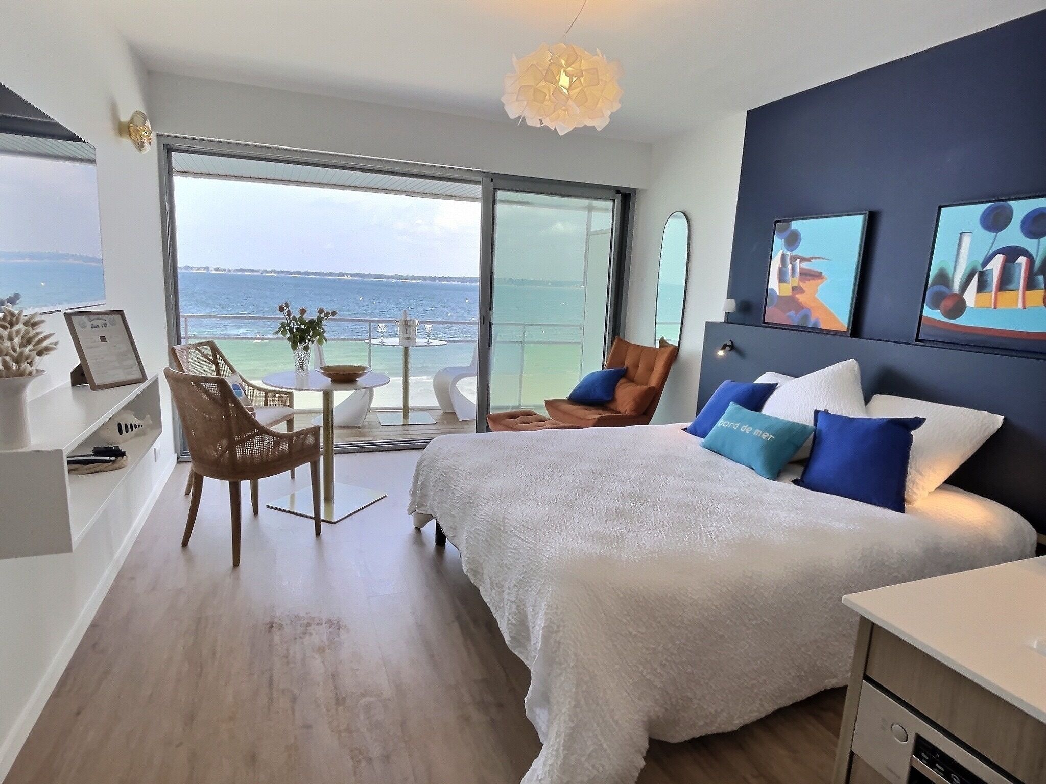 A modern bedroom with a large bed, a dining area, and a balcony with a view of the sea.