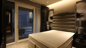 A modern hotel room with a large bed, a sliding glass door to a balcony, and a large wall-mounted artwork. - Luxurious Three Bedroom Flat in Chelsea Creek (London)
